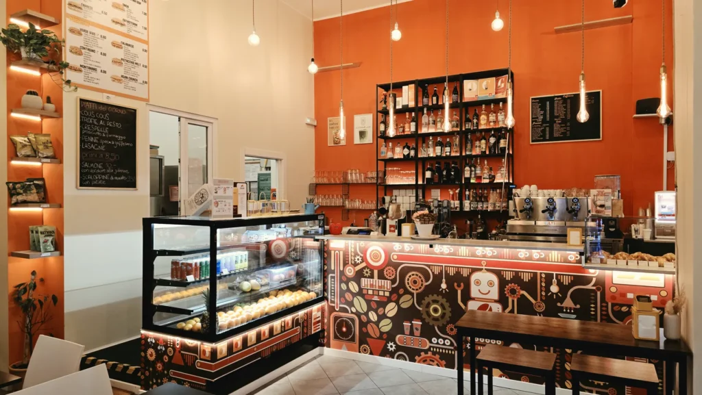 Sala di Astro Cafè con parete arancione, scaffale e vetrina dei dolci